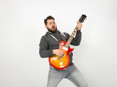 cool man with black hair and beard wearing grey hoodie playing electric guitar in front of white background
