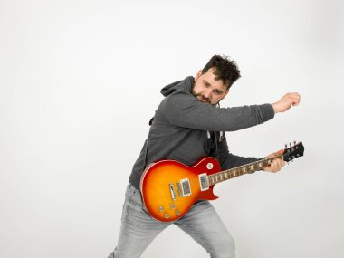 cool man with black hair and beard wearing grey hoodie playing electric guitar in front of white background