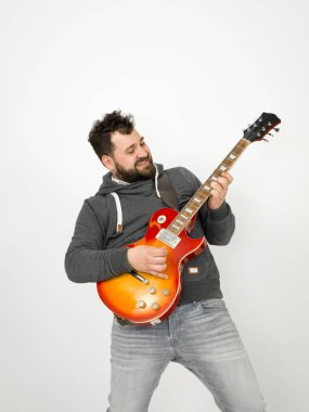 cool man with black hair and beard wearing grey hoodie playing electric guitar in front of white background