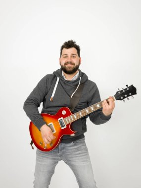 cool man with black hair and beard wearing grey hoodie playing electric guitar in front of white background