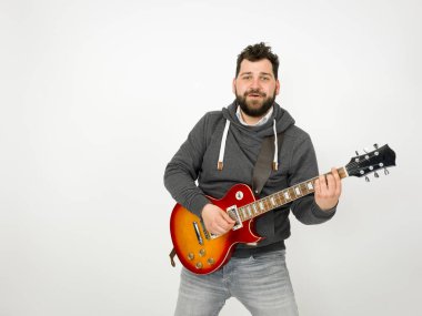 cool man with black hair and beard wearing grey hoodie playing electric guitar in front of white background