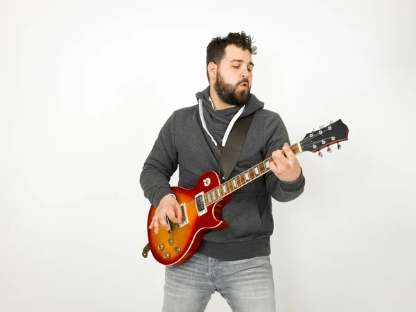 cool man with black hair and beard wearing grey hoodie playing electric guitar in front of white background