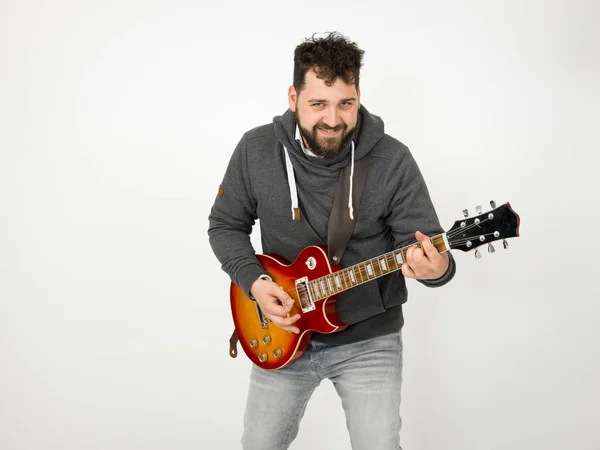 cool man with black hair and beard wearing grey hoodie playing electric guitar in front of white background