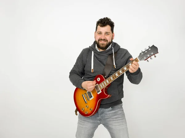 cool man with black hair and beard wearing grey hoodie playing electric guitar in front of white background