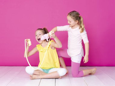 pembe arka plan önünde ev yapımı inceler ile oynarken eğlenen kız kardeşler 