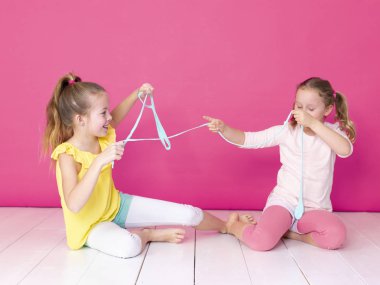 pembe arka plan önünde ev yapımı inceler ile oynarken eğlenen kız kardeşler 