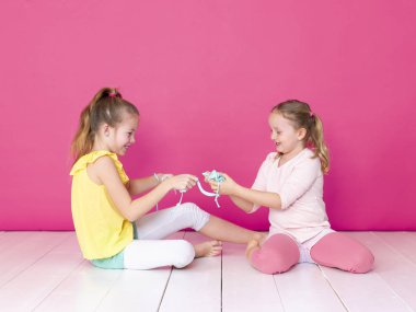 pembe arka plan önünde ev yapımı inceler ile oynarken eğlenen kız kardeşler 
