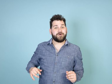 mavi duvar arka plan önünde poz verirken siyah saçlı ve siyah sakallı grimacing ile serin ve genç adam 