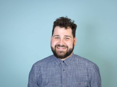 mavi duvar arka plan önünde poz verirken siyah saçlı ve siyah sakallı serin ve genç adam gülümseyen 