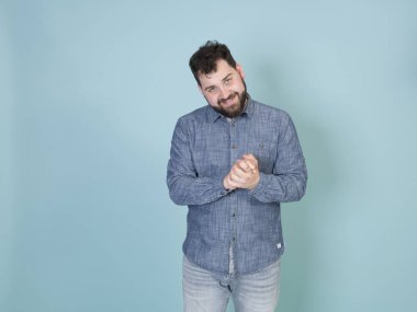 Siyah saçlı ve siyah sakallı kurnaz orta yaşlı bir adam mavi duvar arkasında poz verirken kameraya yeni bir kurnazlıkla bakıyor. 