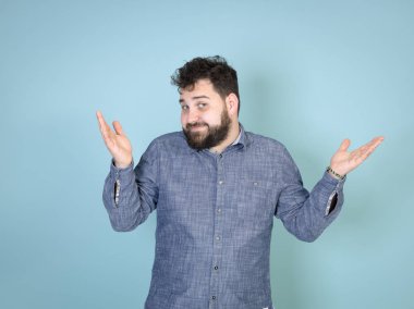 şaşırmış sakallı adam ayrı elleri ile ayakta ve mavi duvar arka plan önünde kamera bakıyor 