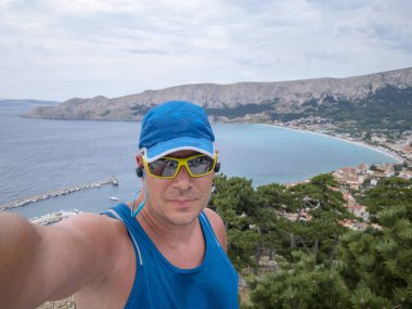 Hırvatistan 'ın Krk adasındaki Baska adasında spor giyim ve güneş gözlüklü izci selfie' si 