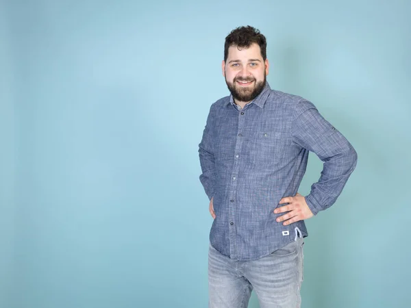 cool and young man with black hair and black beard smiling while posing in front of blue wall background