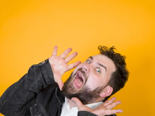 emotional man with black beard in white shirt and black jacket grimacing while posing in front of on studio orange background