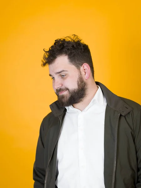 tired man with black beard and black hair in white shirt and black jacket posing on studio orange background