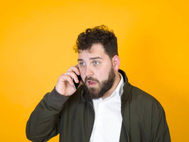 ciddi sakallı adam akıllı telefonda konuşuyor ağzı açık ve gözleri turuncu arka planda. 