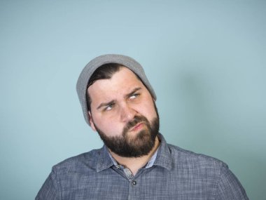 Sakallı, gri şapkalı ve kot gömlekli, mavi duvar arkasına bakan yakışıklı adamın portresi. 