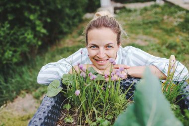 Bahçe yatağının ve taze sebzelerinin yanında poz veren güzel bir kadın.