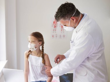Ağız maskeli doktor ağız maskeli kıza iğne yapıyor.