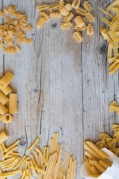 different kinds of egg noodles and yellow pasta on wooden background