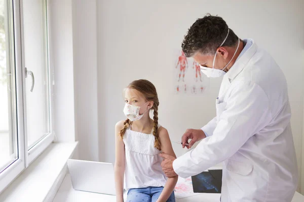 Doctor with mouth mask gives injection to girl with mouth mask