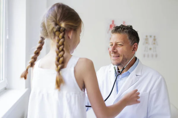 male doctor with three-day beard examines young girl with a stethoscope