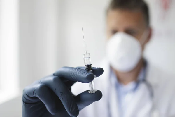 Doctor with nose and mouth mask holds syringe with the remedy against covid 19