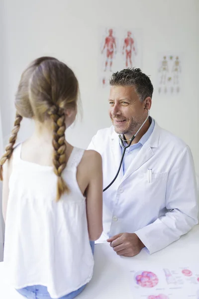 male doctor with three-day beard examines young girl with a stethoscope