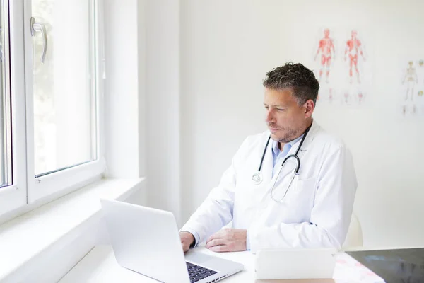 Portrait of a male doctor in his practice with a three-day beard and white coat