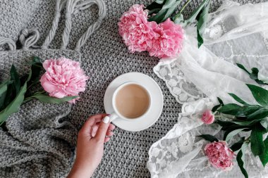 bir fincan kahve ile peonies gri bir arka plan üzerinde tutan kız