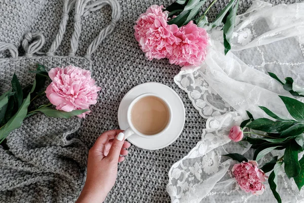 bir fincan kahve ile peonies gri bir arka plan üzerinde tutan kız