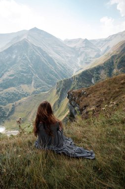 Uzun elbiseli güzel genç kadın uçurumdan Dağları arka planda oturuyor