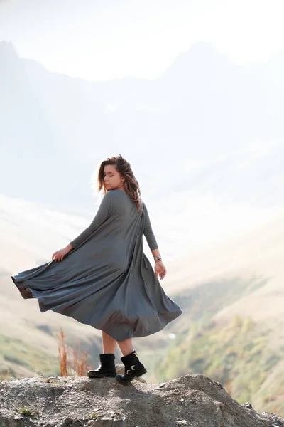 Una hermosa chica en un vestido volador está de pie junto a un acantilado en las montañas — Foto de Stock