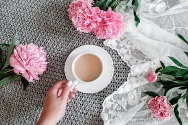 bir fincan kahve ile peonies gri bir arka plan üzerinde tutan kız