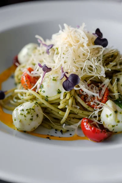 Beyaz bir tabak içinde fesleğen ve mozzarella peynirli spagetti