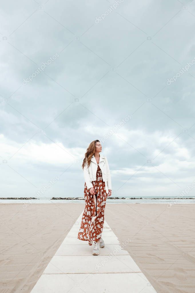 A girl in a flying dress is walking along the coast