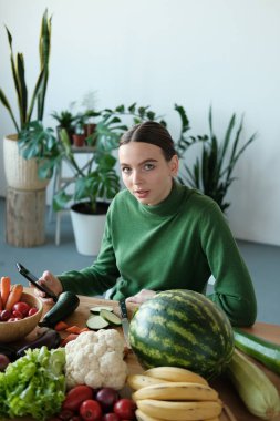 genç vegan kadın ev iç sebzeler ile mutfak masasında telefon kullanarak