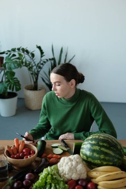 genç vegan kadın ev iç sebzeler ile mutfak masasında telefon kullanarak