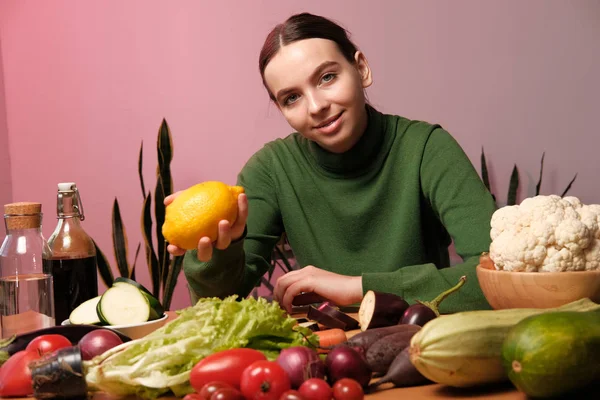 自宅のインテリアで野菜とテーブルでレモンを保持する若い陽気な女の子 — ストック写真