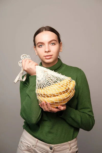 pretty girl holding string bag with bananas in home interior