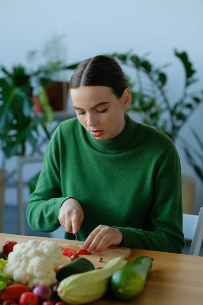 cheerful vegan girl cutting tomatoes with knife in home interior