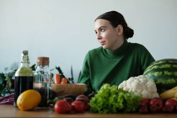 young vegan woman using phone at kitchen table with veggies in home interior