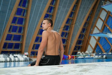 kapalı yüzme havuzunda havuz başında oturan genç erkek yüzücü