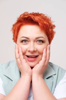 Sade arka planda heyecanlı kızıl saçlı kadının stüdyo portresi.