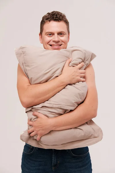 平凡な背景に枕を抱きしめる眠い男のスタジオの肖像画 — ストック写真