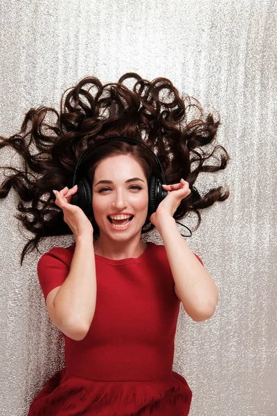 studio portrait of lying woman with headphones and scattered hair on plain background