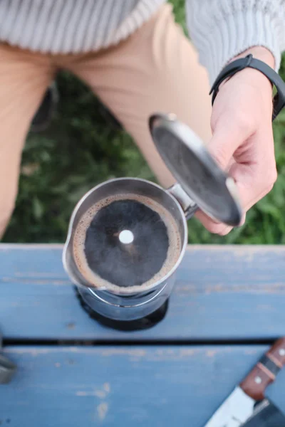 Top view of unrecognizable person opening lid of moka pot coffee maker full of fresh coffee on wooden table outdoors