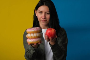 Elinde çörekler ve mavi ve sarı arka planda taze kırmızı elma tutan kararsız bir kadın.