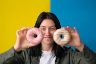 Mavi ve sarı arka planda elinde donut tutan kadın.