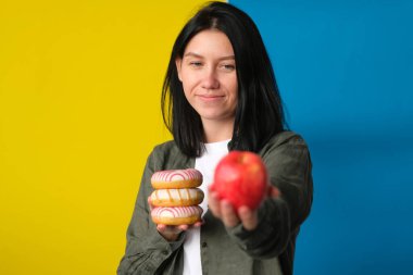 Kadın donut tartıyor ve kırmızı elma mavi ve sarı arka planda